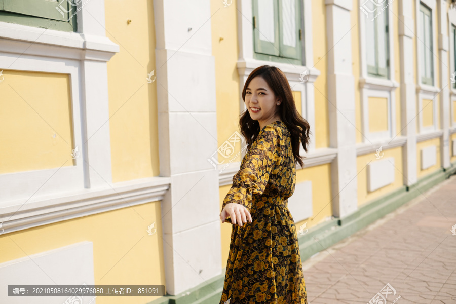 穿着黄色连衣裙的可爱卷曲长发女孩沿着大楼走，转身走到镜头前。