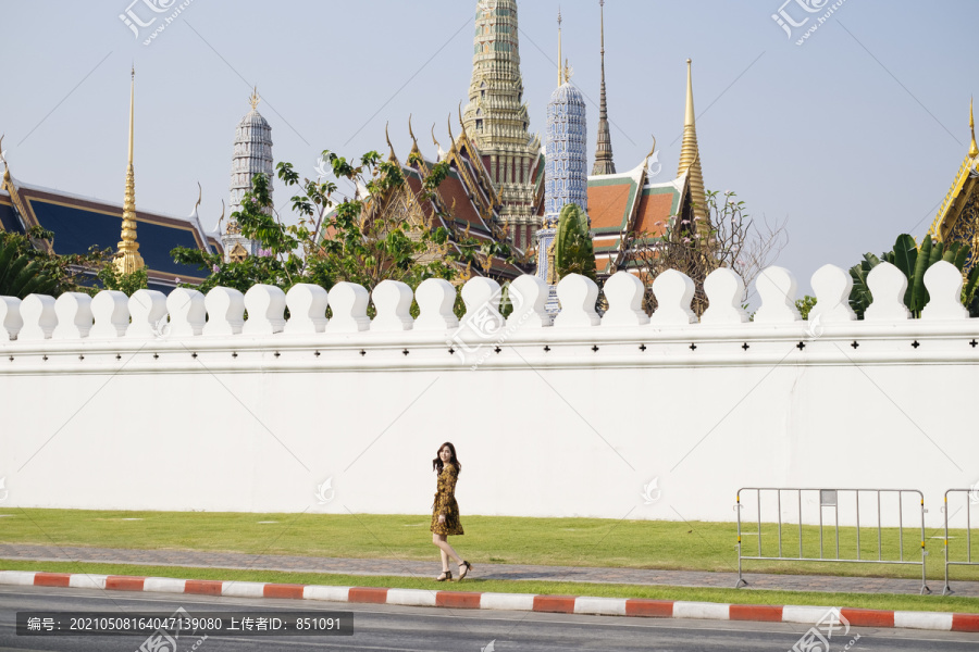 长镜头的可爱卷曲长发女孩穿着黄色连衣裙走在人行道上沿着寺庙的墙壁。
