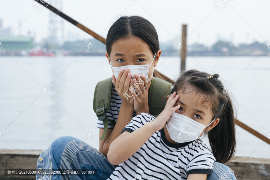 泰国小女孩在户外呆太久头痛。病毒防护概念-戴着防护面具的亚洲小女孩，在雾霾天站在河边。到处都是污染。