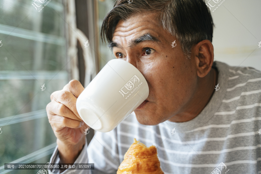 老人一边喝着杯子里的热咖啡，一边用另一只手拿着香肠羊角面包，站在百叶窗边戴着眼镜，他惊讶地发现，他看