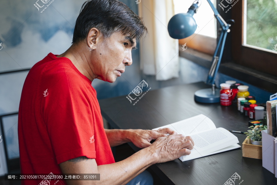 穿红色t恤的老人在靠窗的木桌旁看书。