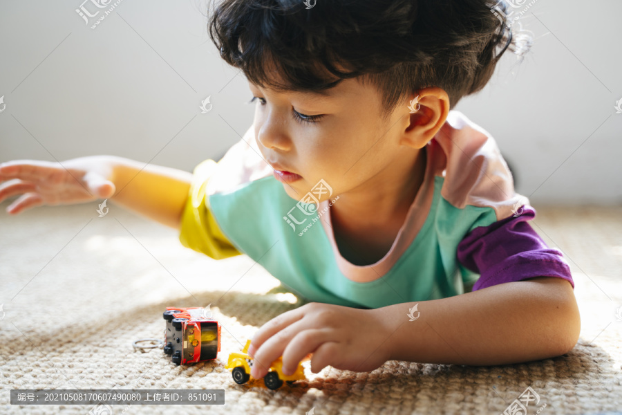 小男孩趴在地板上玩汽车玩具。