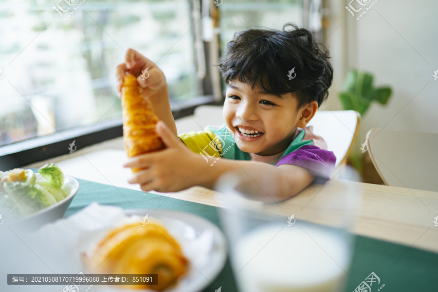 小男孩手里拿着香肠羊角面包，脸上挂着幸福的微笑。