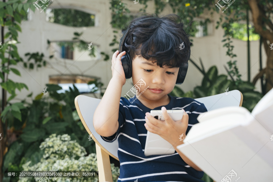 小男孩戴着耳机，拿着智能手机看动画片。
