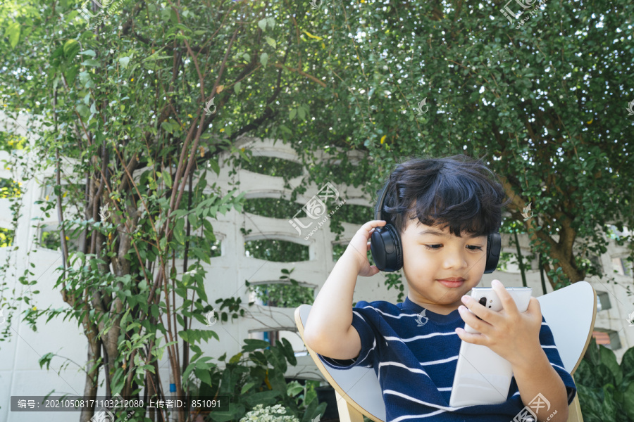 周末，戴着无线耳机的小男孩坐在后院，用智能手机看动画片。