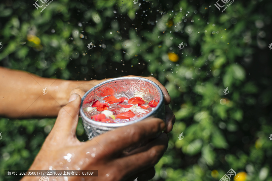 老人的手拿着盛满清水和鲜花的银碗，这是泼水节的剪影。