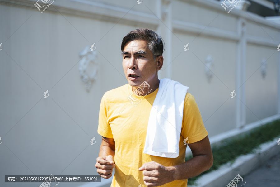 穿着黄色t恤的老人在夏天的早晨用白毛巾慢跑。