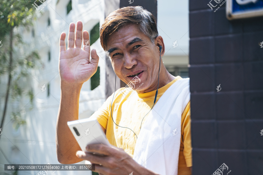 穿着黄色t恤衫的老人站在家门前向邻居挥手致意。