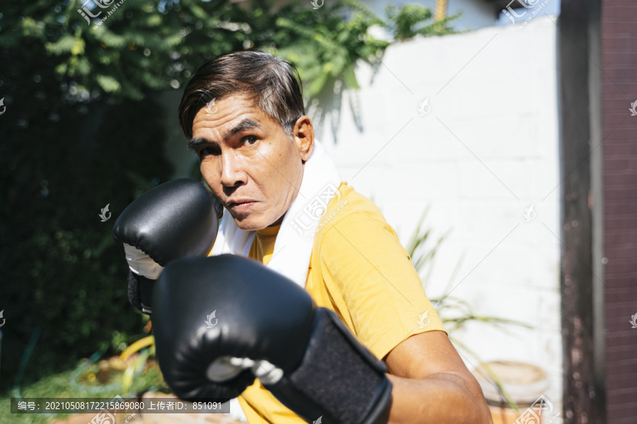在阳光明媚的日子里，老人一个人在家里接受拳击训练。