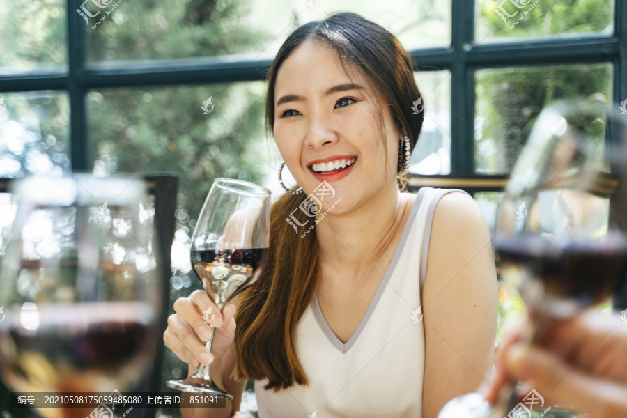 开朗快乐的亚洲女人穿着白色连衣裙，和朋友一起享受聚会，举着酒杯，和朋友聊天。