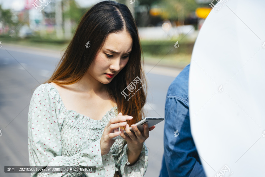 愤怒的亚洲女人开始用电话打电话给机械师来这里修车。年轻女子一边用手机一边看着街上抛锚的汽车。