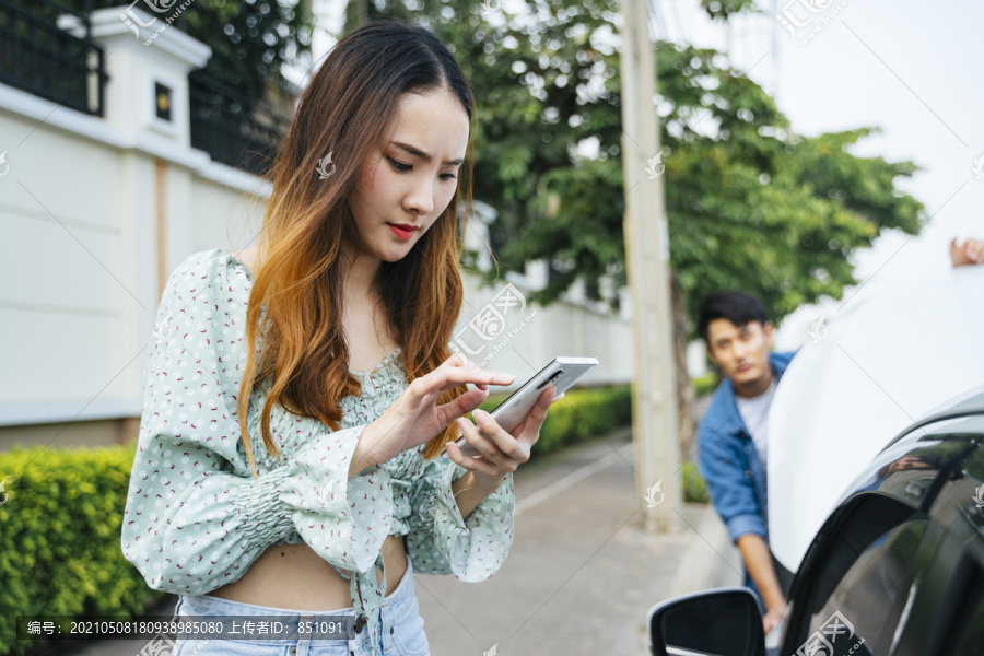 愤怒的亚洲女人开始用电话打电话给机械师来这里修车。年轻女子一边用手机一边看着街上抛锚的汽车。