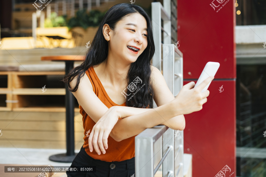 快乐快乐的亚洲美女穿着橙色衬衫，用智能手机和朋友聊天，视频通话，上网。