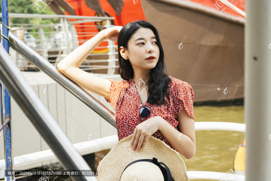 年轻美丽的泰国亚裔旅行家妇女在朝普拉亚河穿着红色连衣裙的画像。