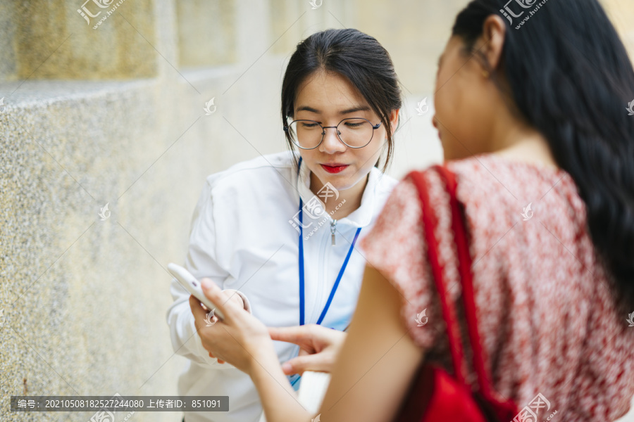 美丽的亚洲导游女士在街上用智能手机给旅行者指路。