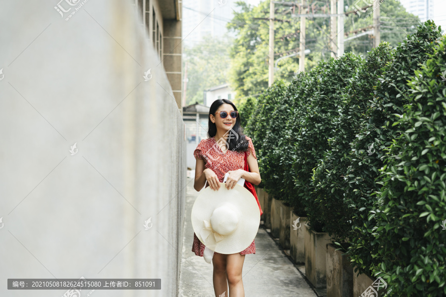 美丽的亚洲游客穿着红色的衣服戴着太阳镜戴着帽子走在街巷。