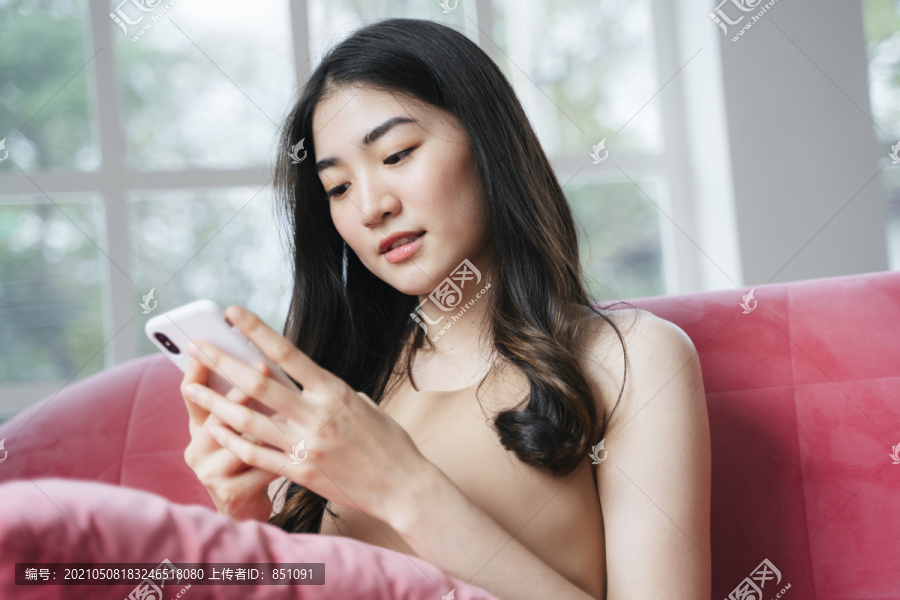 卷发女孩坐在粉色沙发上，用智能手机按男友的电话号码，然后给他打电话。