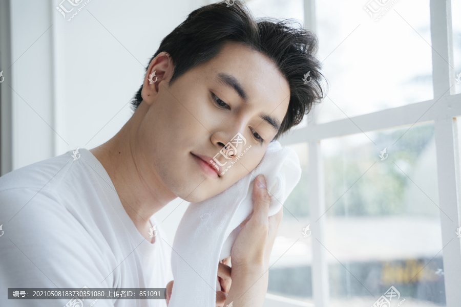一个穿白色t恤衫的男人用毛巾洗完脸后擦了擦。