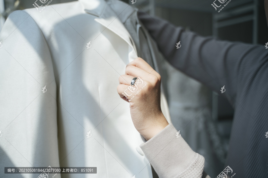一个男人来到婚礼工作室挑选他的婚纱并试穿，一个男人手上的戒指夹在无名指上，同时抓住衣领。