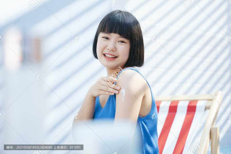 漂亮可爱漂亮的鲍勃发型亚洲女人在蓝色背心衬衫应用紫外线乳液霜保护肩膀。使用乳霜乳液。商业用途。