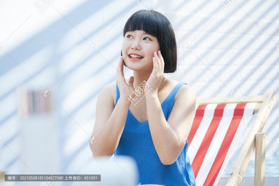 快乐美丽的亚洲女人美丽的鲍勃发型穿着蓝色背心衬衫的亚洲女人在白色房间的脸上涂奶油乳液。