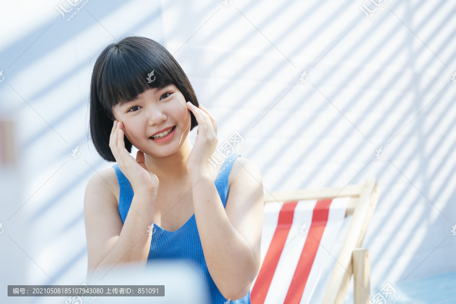 快乐美丽的亚洲女人美丽的鲍勃发型穿着蓝色背心衬衫的亚洲女人在白色房间的脸上涂奶油乳液。