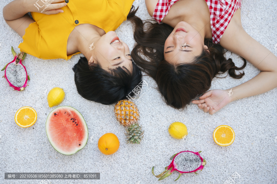 两位亚洲女性密友暑假躺在地上。热带水果。顶视图。穿黄衬衫和红衬衫的亚洲女人。旅游度假。假日周末。