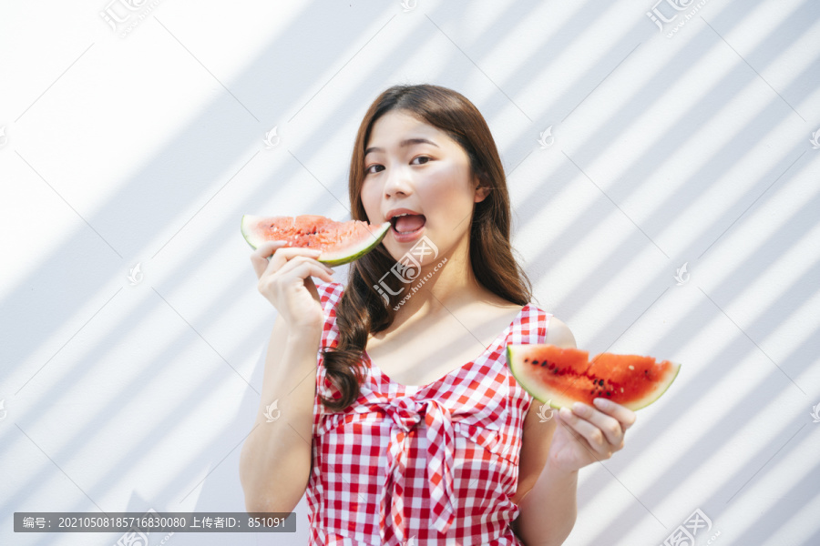 一位穿着红裙子的亚洲美女手里拿着一块西瓜。漂亮的亚洲女人喜欢吃西瓜。在白色背景上。