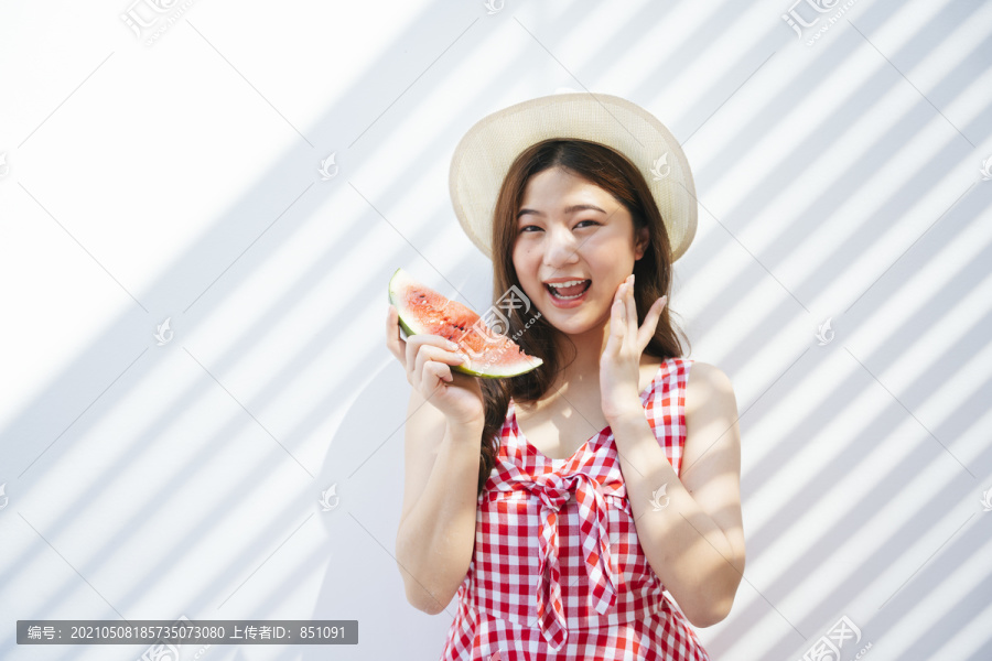 一位身穿红色连衣裙的亚洲年轻女子在背景上吃着新鲜的西瓜。带着水果的快乐女人。