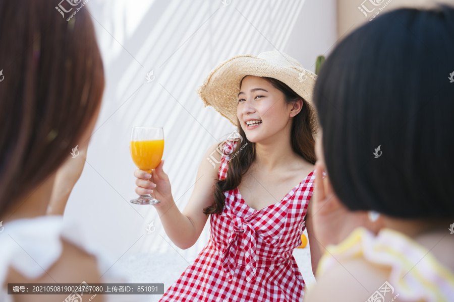 美丽的亚洲年轻女子戴着帽子，穿着红裙子，和朋友在夏日派对上喝着橙汁。