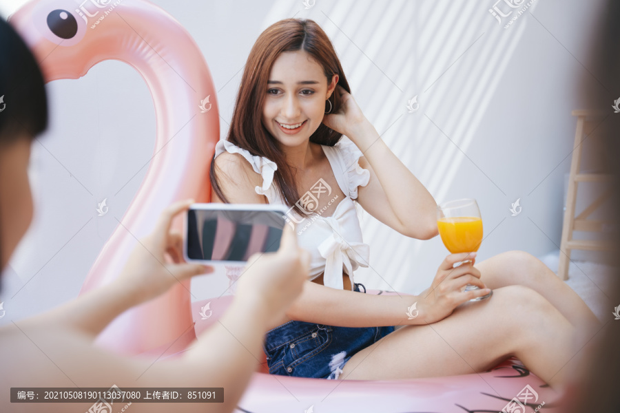 朋友用智能手机拍照，性感女人拿着橙汁坐在游泳圈上。