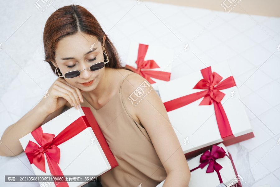 戴着墨镜的美女坐在白色沙发沙发上一堆礼盒里。礼物盒和年轻漂亮的女孩。