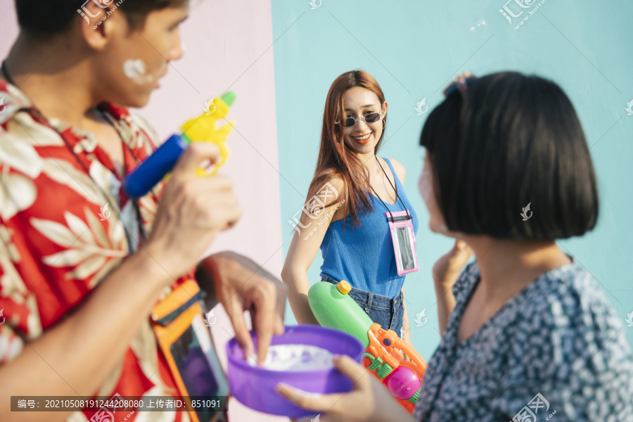 在泰国曼谷，穿着蓝色背心衬衫、戴着墨镜的性感外国人和当地人一起玩泼水。在柔和的粉蓝色背景上孤立。