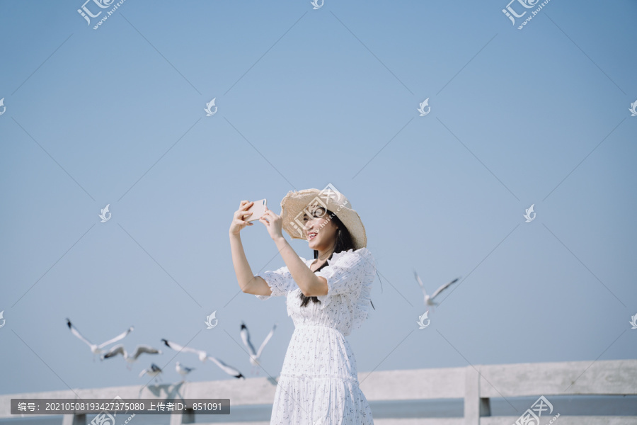 长发白衣白帽女子兴奋地用智能手机为迁徙季节的海鸥拍照。