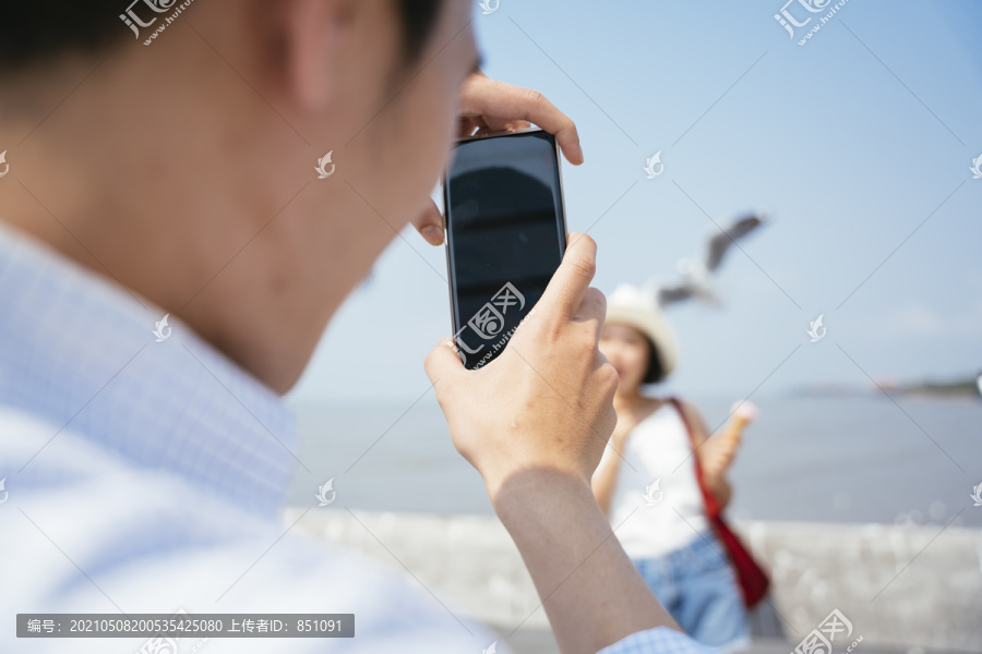 摄影师一名男子用智能手机拍下一名女子在海边拿着冰激凌。为blog和vlog制作内容。旅游理念。