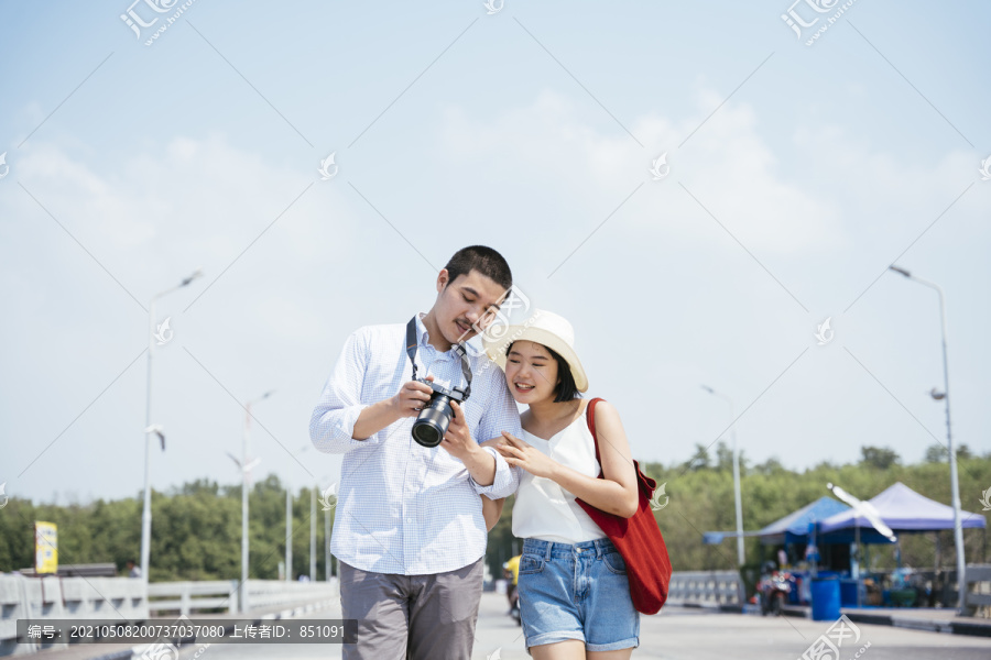 亚泰夫妇走在海边大桥上看镜头。一对幸福的旅游情侣在相机里看照片。