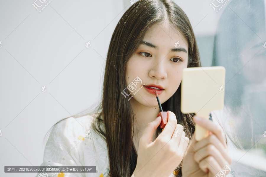 美丽的亚洲年轻的泰国妇女做化妆前使用唇膏在镜子前。