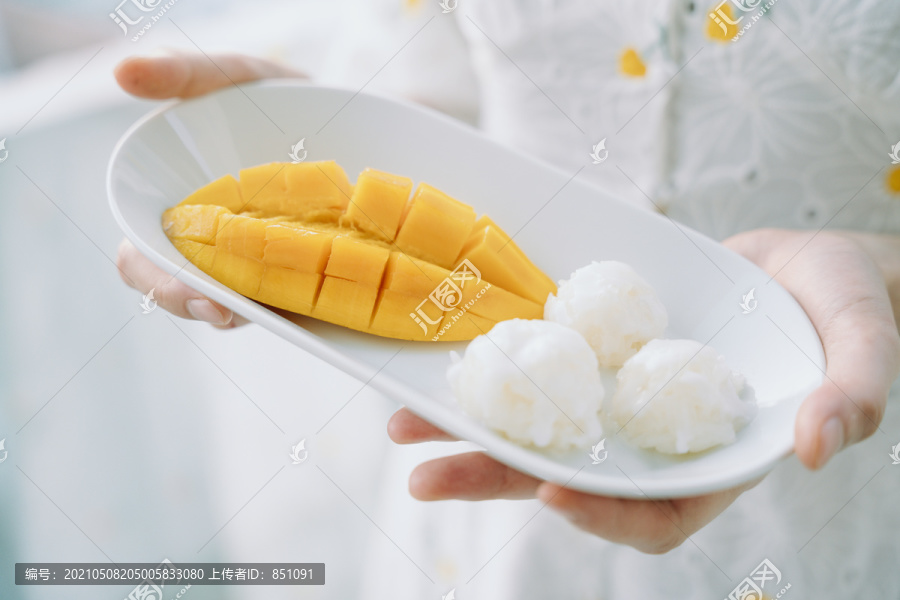 芒果糯米放在女人手里的白色盘子里。