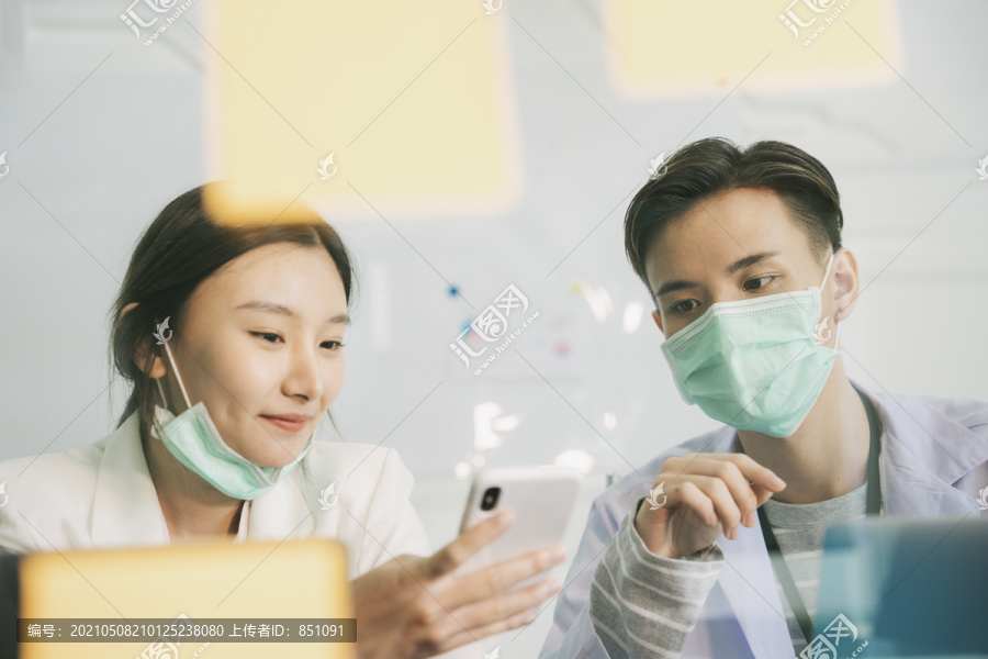 医生和护士在午休时间交谈，他们在医院房间里看着智能手机。