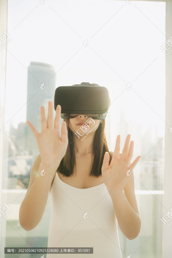 特写美丽的亚泰女子戴着VR耳机，玩虚拟现实游戏。游戏行业的技术。在摩天大楼背景上。