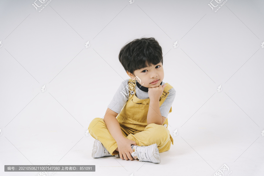 穿着黄色工作服的小男孩坐在工作室白色背景前。