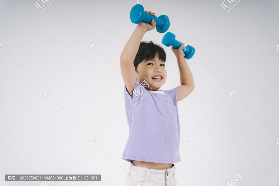穿着紫色t恤的小男孩快乐地玩着蓝色的小哑铃。