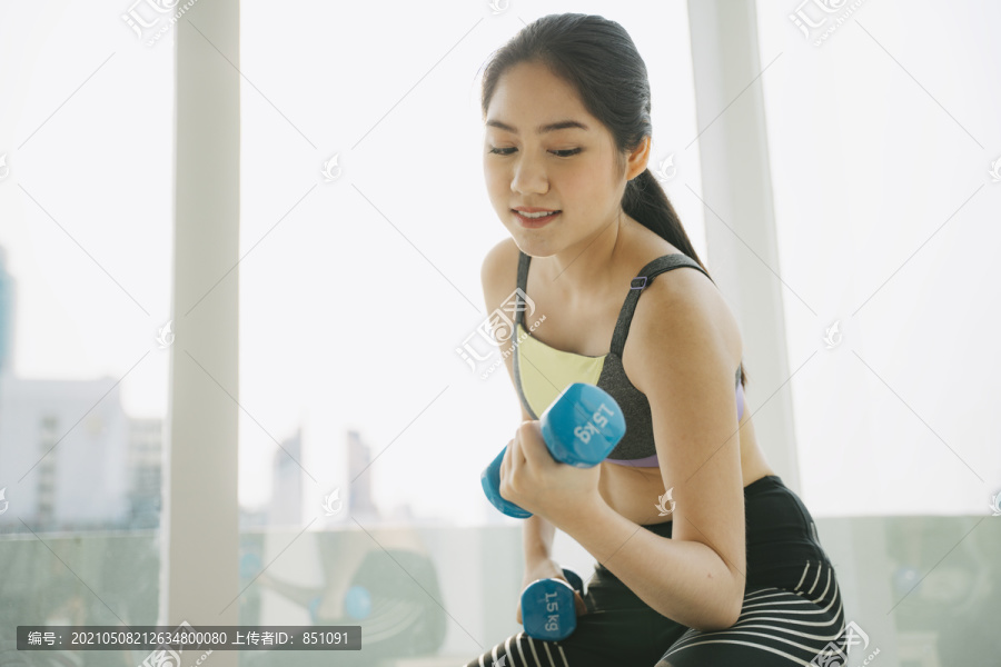 因为体育馆关门了，所以隔离期间妇女穿运动服在家锻炼身体。在家里用蓝色哑铃训练。