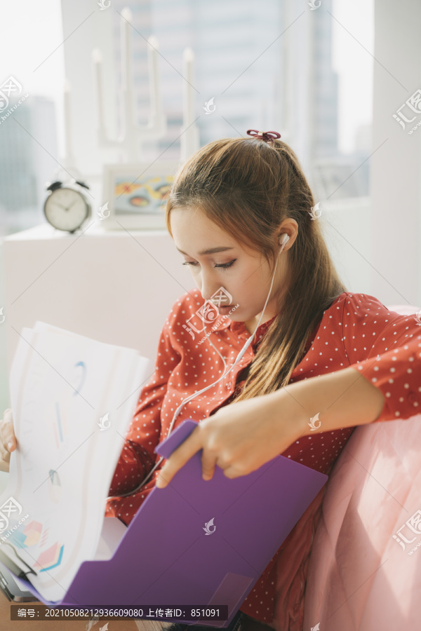 在家工作的概念-穿着红色睡衣衬衫的漂亮年轻女子坐在沙发上在家里写文件报告。检疫。