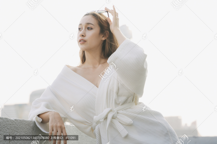 复制空间-性感的年轻女子穿着白色浴袍在公寓阳台上的城市背景。