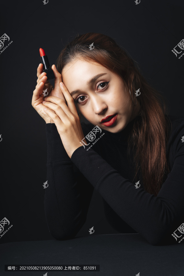 在黑暗的背景下，穿着黑色毛衣的漂亮年轻女子的特写肖像。黑暗中的美。手上涂着红色唇膏的女人。