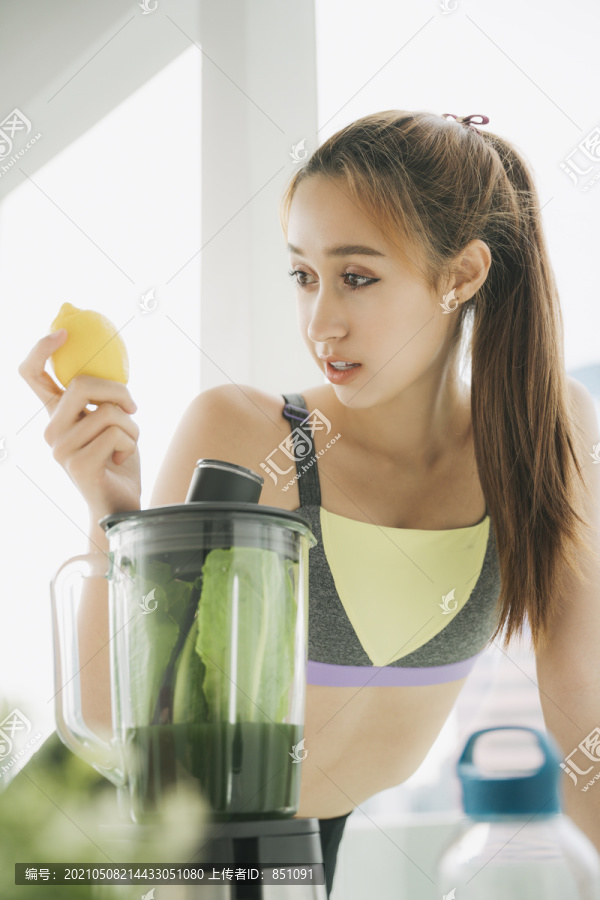穿着运动内衣的健康年轻女子在厨房用榨汁机勾兑新鲜蔬菜汁，准备营养丰富的维生素包装饮料。健康饮食，素食