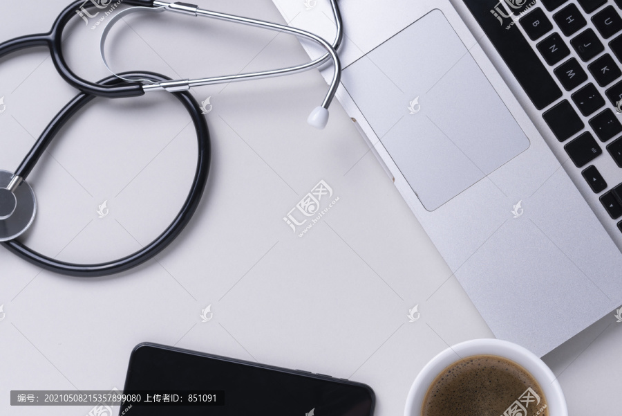 顶视图-医生工作台，配有听诊器、笔记本电脑、书本和灰色背景上的眼镜。