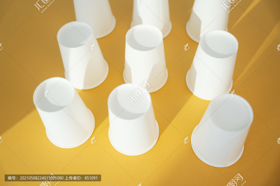 正面朝下的九个纸杯呈正方形，背景为橙色。