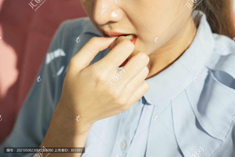 亚洲女人咬指甲。穿着正式衬衫的忧心忡忡的女人的肖像。